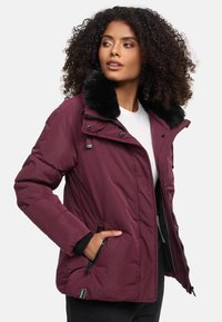 Bordeaux pufferjack met een faux fur kraag, voorzien van ritszakken, een volledige ritssluiting en een gewatteerde textuur.