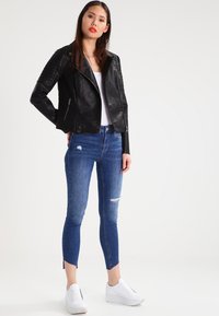Black leather biker jacket with quilted shoulders, paired with blue skinny jeans featuring ripped details and white sneakers.