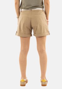 Shorts beige in misto cotone con risvolti, tasche sul retro e una cintura bianca a fantasia. Indossati con sneakers multicolori a taglio basso.