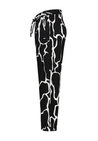 Pantalons noir et blanc avec un motif en tache de vache, taille élastique avec cordon de serrage et poches latérales. Texture de tissu lisse.