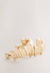 Gold-tone hair clip with a wavy design, featuring ridged and smooth sections. Material appears metallic with a shiny finish.
