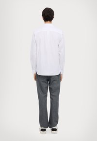 White long-sleeve shirt with a buttoned collar, paired with loose-fit gray jeans and white sneakers featuring black accents.