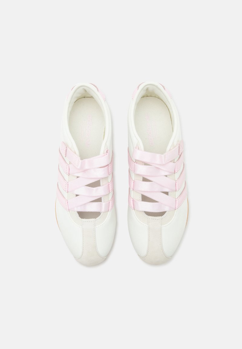 Witte sportschoenen met roze kruisvormige elastische veters en afgeronde neuzen, van bovenaf getoond op een effen witte achtergrond.