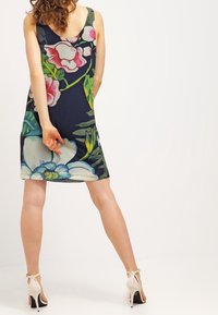 Mönstrad ärmlös klänning i marinblått med livfulla gröna, rosa och vita mönster. Knytande tyg, knälång och rund halsringning.
