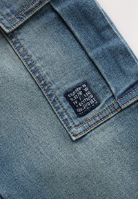 Gros plan sur un tissu en denim bleu présentant une petite étiquette noire avec du texte blanc et des coutures orange visibles le long des coutures.