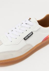 Weißer Sneaker mit Wildleder- und Gummidetails, ausgestattet mit weißen Schnürsenkeln, einem schwarzen Etikett mit der Aufschrift "STEVE MADDEN" und einer strukturierten Gummisohle.