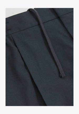 Ciemnoniebieskie spodnie z zakładkami i elastycznym paskiem ze sznurkiem, wykonane z teksturowanej tkaniny, która jest gładka i gęsto tkana.