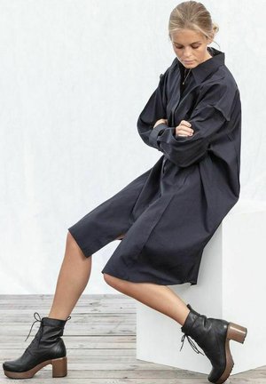 Navy oversized shirt dress with long sleeves and side slits. Worn with black lace-up ankle boots featuring wooden block heels.