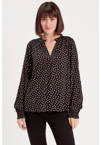 Black long-sleeve blouse with a polka dot pattern in beige, featuring a v-neckline and gathered cuffs for a relaxed fit.
