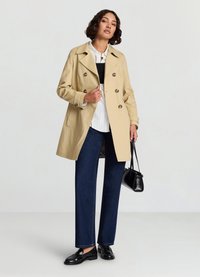 Trench-coat beige à double boutonnage avec des boutons marron, accompagné d'un haut noir et d'un pantalon en denim bleu. Mocassins noirs et sac à main.