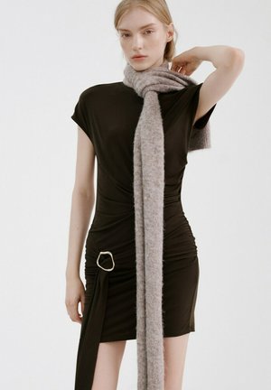 Mujer con un vestido negro ajustado con un detalle de hebilla plateada y una bufanda larga y gruesa de color gris enrollada alrededor del cuello.