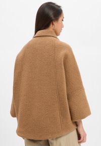Brown wool-blend coat with a structured shape, large collar, and wide sleeves. Soft texture with visible seams, showcasing a modern design.