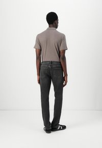 Camisa polo gris de mangas cortas, combinada con jeans gris oscuro. Diseño simple con pierna recta, llevada con zapatillas negras con rayas blancas.