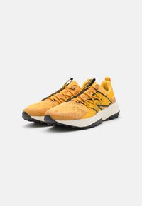 Baskets de sport jaunes avec une tige en mesh et en synthétique, comportant des accents noirs, une surface texturée et une semelle extérieure noire robuste pour une meilleure traction.