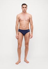 Sunga de banho azul-marinho com uma textura suave e detalhe do logótipo no lado esquerdo. O tecido é elástico, ajustado ao corpo e projetado para conforto.