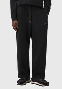 Schwarze Jogginghose aus Fleece mit Kordelzug in der Taille, gerippten Bündchen und seitlichen Taschen. Verfügt über ein dezentes, aufgesticktes Logo am Oberschenkel.