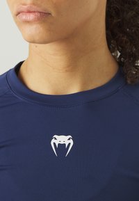 Șoar de sport bleumarin cu un logo alb de cobră pe piept, realizat dintr-un material neted și elastic, cu guler rotund și mâneci scurte.