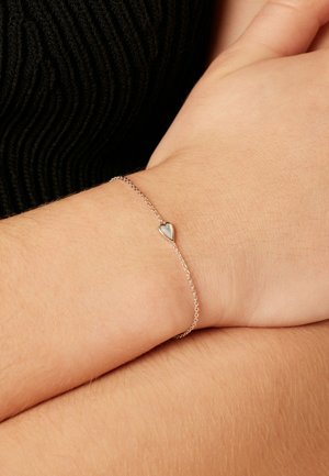 Zilveren armband met een klein hartjesbedel, fijne kettingontwerp en minimalistische stijl, liggend op een lichtgekleurde pols.