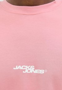Rozā kokvilnas T-krekls ar apaļu apkakli un baltu logo, kas uz burtiem "JACK & JONES" ir drukāts priekšpusē.