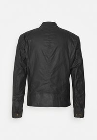 Czarna kurtka wykonana z gładkiej, lekko teksturowanej tkaniny. Posiada stojący kołnierz i mankiety zapinane na guziki o minimalistycznym wzornictwie. Widok z tyłu.