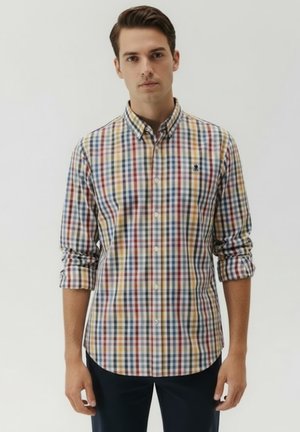 Camicia button-up con un motivo a quadri multicolore in blu, rosso, giallo e bianco. Maniche lunghe arrotolate a metà avambraccio.