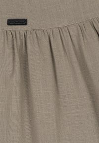 Tessuto beige con una texture morbida e un aspetto leggermente stropicciato. Presenta un design arricciato in vita e un'etichetta con logo nera.