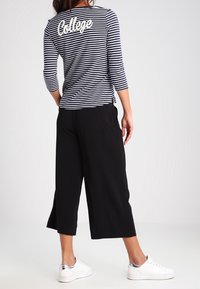 Mörkblå och vit randig skjorta med trekvartslånga ärmar som har "College" i vitt på ryggen. Kombineras med svarta culotter och vita skor.