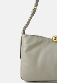 Szara skórzana torba na ramię z regulowanym paskiem i złotym kulistym zapięciem w prawym górnym rogu.