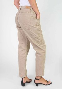 Beige cargobroek van katoen, met meerdere zakken, een relaxte pasvorm en subtiele stiksels. Draag ze met zwarte hoge sandalen.