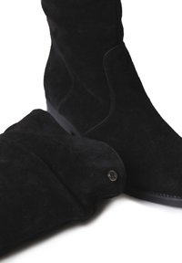 Stivali alti neri in suede con finitura testurizzata, dotati di suola piatta e dettaglio con bottone sul lato.