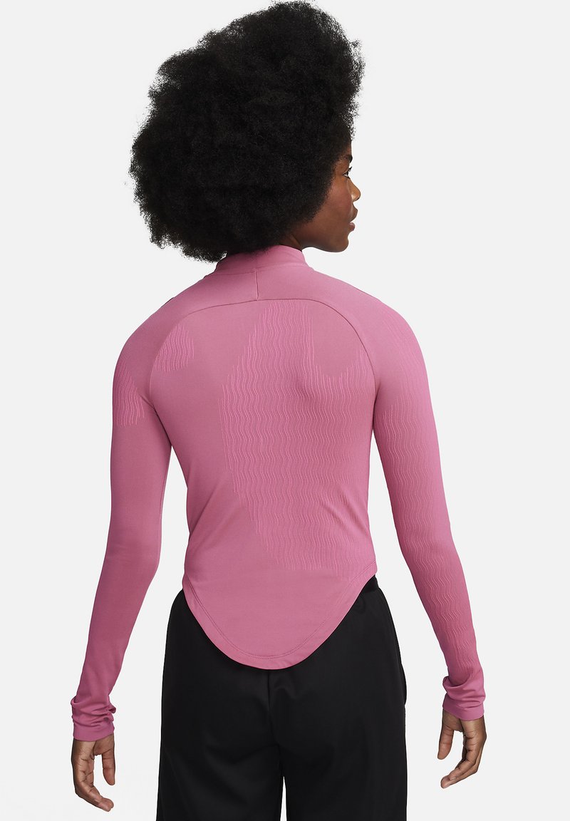Camiseta deportiva de manga larga en tejido rosa claro con una textura suave, cuello alto y sutil patrón de ondas en la parte posterior.