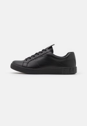 Baskets basses en cuir noir avec lacets, détails de couture et nom de marque embossé sur le côté et la semelle du talon.