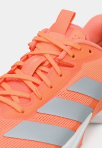 Φωτεινό κοραλλί αθλητικό παπούτσι με γκρι ρίγες, επάνω μέρος από δίχτυ, και σφιχτά δεμένα κορδόνια με θηλιά στο γλωσσάκι.