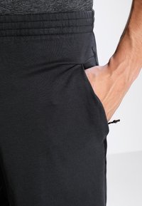 Pantalones deportivos negros con una textura suave, cintura elástica con costuras horizontales y detalle de mano en el bolsillo para mayor utilidad.