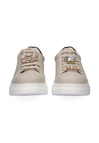 Zapatillas beige con una textura suave, que presentan acentos decorativos: un gran cristal y un adorno de mariposa en los cordones. Suela blanca.
