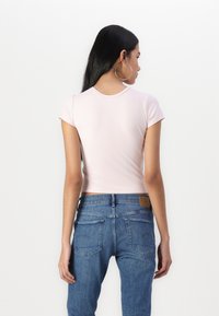 Lys rosa tettsittende t-skjorte med korte ermer, glatt tekstur; kombinert med høyhælte blå denimjeans med baklommer og et lærmerke.