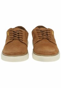 Zapatos de ante marrón con una superficie texturizada, que cuentan con cordones, una suela de goma blanca y un sutil detalle de marca en el lateral.