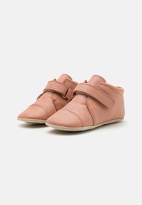 Roza usnjena čevlja z velcro trakom, zasnovo koničastih prstov in textured površino. Mehka bež podplat z minimalnimi šivi.
