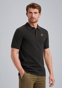 Zwarte polo met korte mouwen van een textuurgebreide stof, met een kraag en een klein logo-opdruk op de linker borst.