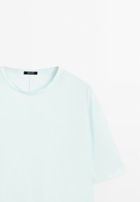 Světlemodré tričko s krátkým rukávem vyrobené z měkké tkaniny. Má kulatý výstřih a uvnitř štítek s názvem značky, minimalistický design.