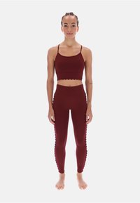 Burgundowy zestaw odzieży sportowej składający się z krótkiego topu z falbaniastym dołem oraz dopasowanych legginsów o wysokim stanie z falbaniastymi akcentami po bokach.
