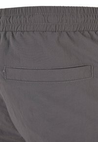 Shorts gris avec une taille élastique, dotés d'une poche arrière rectangulaire avec des coutures horizontales et d'une texture lisse et légère.