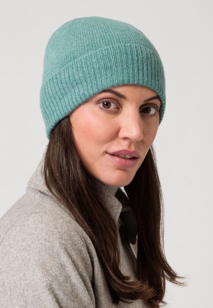 Maglione a coste in teal realizzato in materiale morbido, dalla forma aderente e texture liscia, indossato con un maglione grigio con colletto.