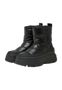 Botines negros hasta el tobillo con una textura acolchada, fabricados en material sintético, con una suela gruesa y acanalada y un logo en el lateral.
