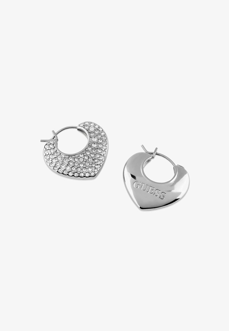 Orecchini a cerchio a forma di cuore in argento, uno con decorazioni in strass e l'altro inciso con "GUESS." Texture liscia con finitura lucida.