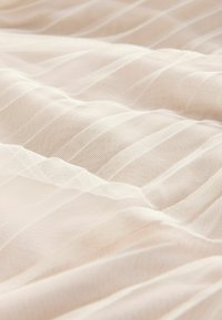 Hellbeige Stoff mit einer durchsichtigen, strukturierten Oberfläche und dünnen vertikalen Streifen, die weiche Falten und subtile Transparenz zeigen.