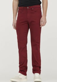 Pantalon en denim rouge avec une coupe slim, doté d'une fermeture à bouton et à glissière, d'une texture subtile et de poches avant. Associé à des baskets blanches.