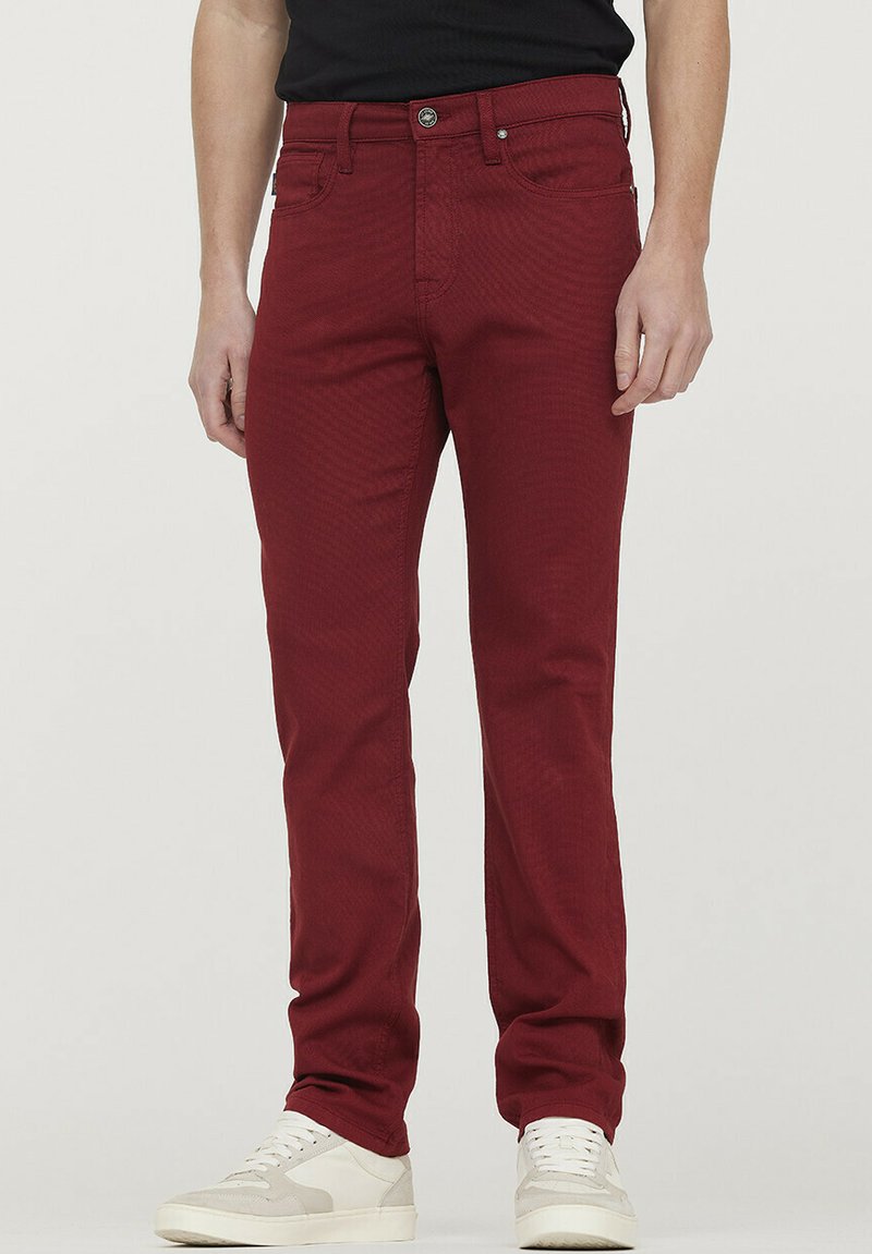 Pantalon en denim rouge avec une coupe slim, doté d'une fermeture à bouton et à glissière, d'une texture subtile et de poches avant. Associé à des baskets blanches.