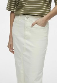 Falda de mezclilla blanca con una silueta ajustada, bolsillo lateral y costuras en contraste. Combinada con una blusa de rayas en verde oliva.