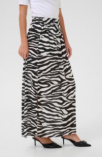 Jupe maxi avec un motif zèbre noir et blanc, fabriquée en tissu léger avec une taille smockée et une fente sur un côté. Associée à des talons noirs.
